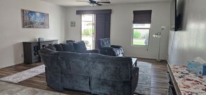 Ein Wohnzimmer mit einem dunkelgrauen Sofa, einer kleinen Kommode, einer Stehlampe und einem Bild an der Wand.