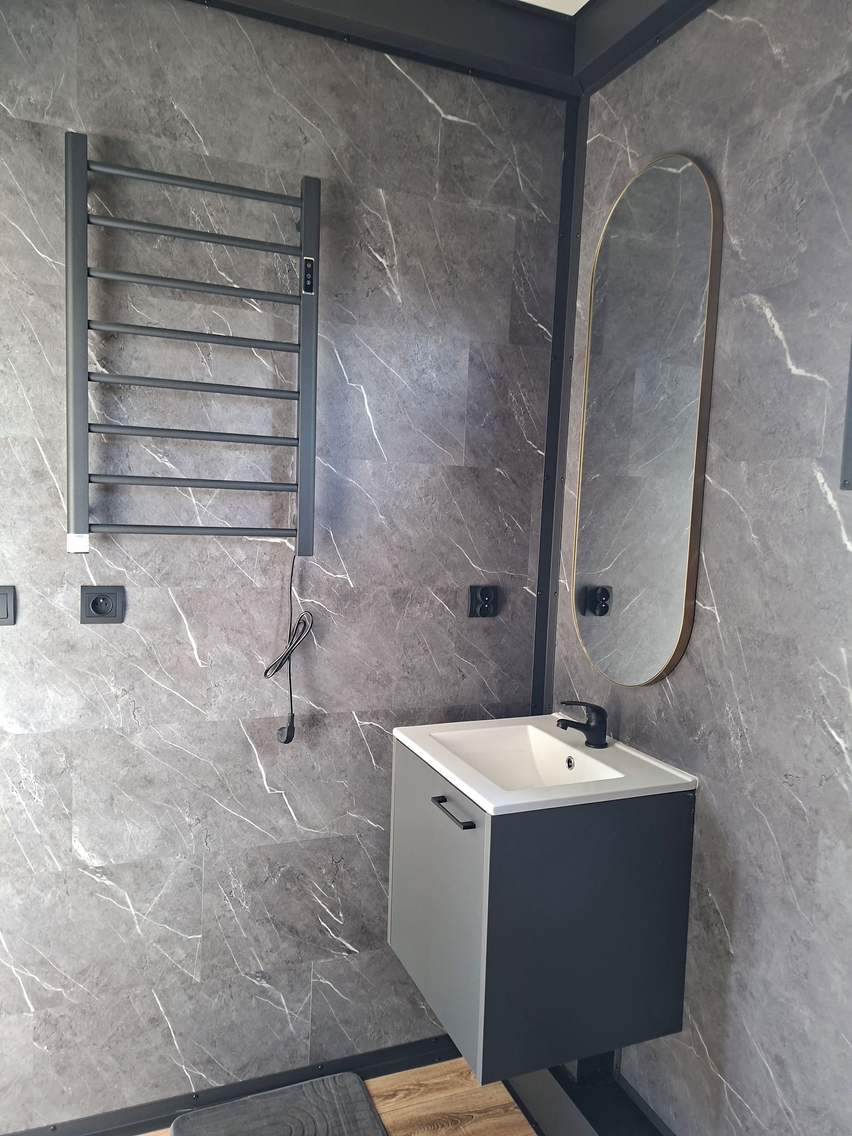 Une salle de bain avec un mur en marbre, un porte-serviettes, un miroir et un lavabo.