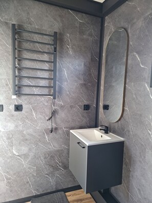 Une salle de bain avec un mur en marbre, un porte-serviettes, un miroir et un lavabo.