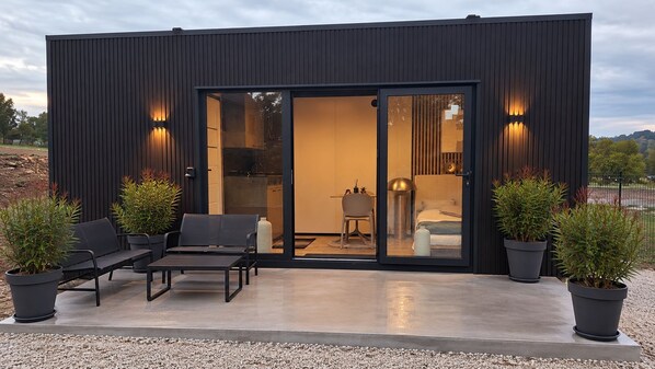 Un bâtiment moderne doté d’une entrée avec une porte-fenêtre coulissante, d’un espace extérieur aménagé pour s’asseoir et de plantes en pot.
