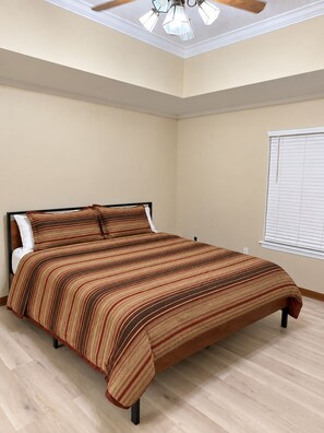 A bedroom with a bed, a ceiling fan, and a window with blinds. - The Southern Standard, Sleeps 6 (Brandon)