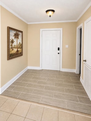 A hallway with beige walls, a white door, and a framed picture of palm trees. - The Southern Standard, Sleeps 6 (Brandon)