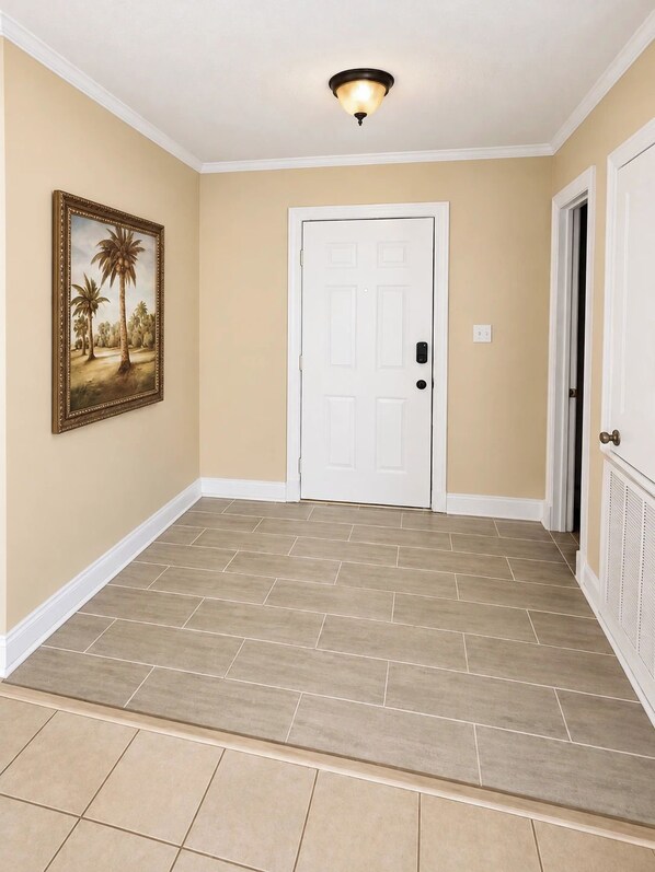 A hallway with beige walls, a white door, and a framed picture of palm trees. - The Southern Standard, Sleeps 6 (Brandon)
