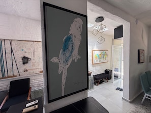 A modern interior with a large framed artwork of a parrot, a black sofa, and a dining area with a glass partition. - Hidden Gem in the Zona. King Bed, Designer Reno. Private yet near It All (Puerto Vallarta)