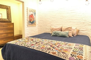 A bedroom with a bed, a dresser, a painting, and a white brick wall. - Hidden Gem in the Zona. King Bed, Designer Reno. Private yet near It All (Puerto Vallarta)