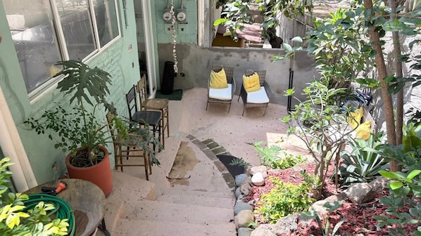 A small outdoor seating area with chairs and a table, surrounded by potted plants and a garden. - Hidden Gem in the Zona. King Bed, Designer Reno. Private yet near It All (Puerto Vallarta)