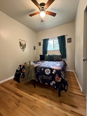 A bedroom with a bed, a ceiling fan, a window with curtains, and a wall decoration. - Mountain and Meadows, family-friendly 3BR, near I-84, parks and dining. (Mountain Home)