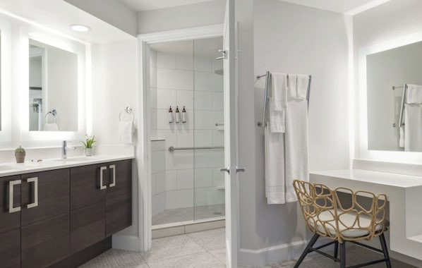 Ein modernes Badezimmer mit begehbarer Dusche, einem Waschtisch mit dunklen Schränken und einem Korbstuhl.