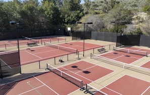 Ein Außen-Tennisplatz mit mehreren Spielfeldern, Bänken und Beleuchtung.