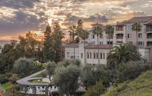 Ein mehrstöckiges Hotel mit Innenhof, umgeben von Bäumen und Blick auf den Sonnenuntergang.