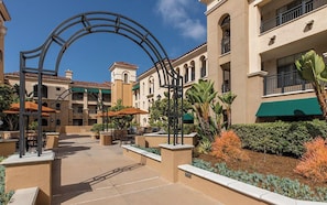 A courtyard with outdoor seating, a central archway, and a building with balconies and a green awning. - Super Bowl, Presidents' Day & Valentine's Week-2BR Villa, Marriott Newport Coast (Newport Beach)