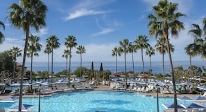 Ein Poolbereich mit Liegestühlen und Sonnenschirmen, umgeben von Palmen, mit Blick auf das Meer.