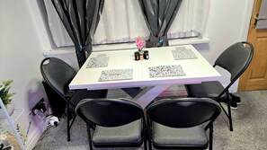 Mesa de jantar com quatro cadeiras, um vaso de flores e uma janela com cortinas.
