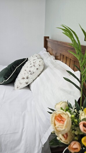 A bed with white bedding and a wooden headboard, a green pillow, a fluffy white pillow, and a bouquet of flowers. - A Cozy 2 Bedroom Apartment Close to NEC & Airport (Birmingham)