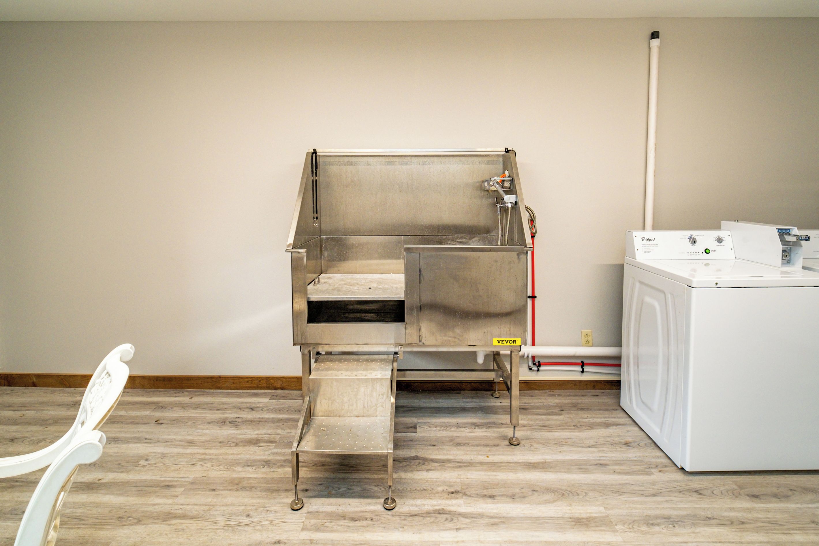 Een kamer met een roestvrijstalen spoelbak, een wasmachine en een stoel.