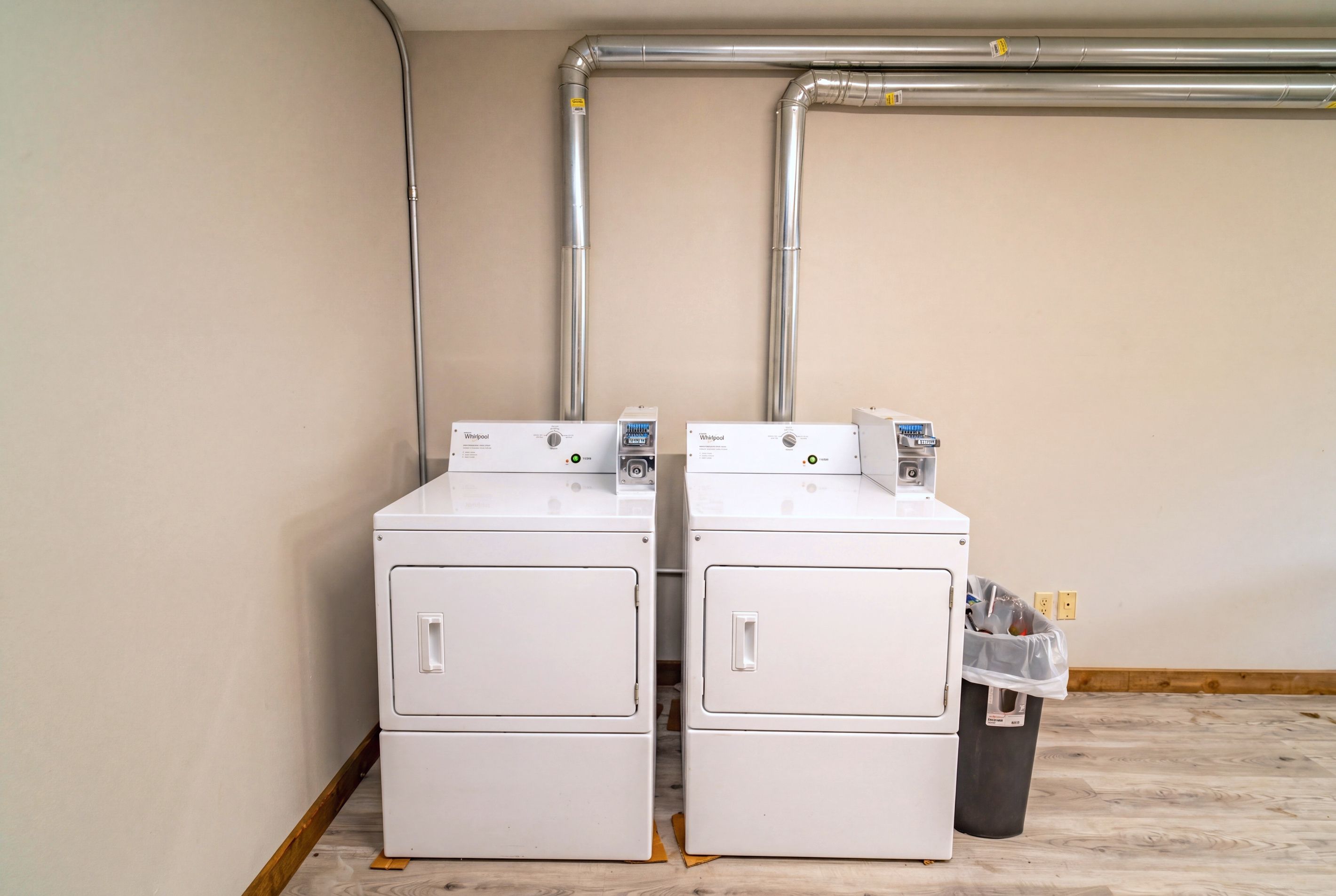 Two stacked white Whirlpool washing machines in a room with beige walls and wooden flooring.