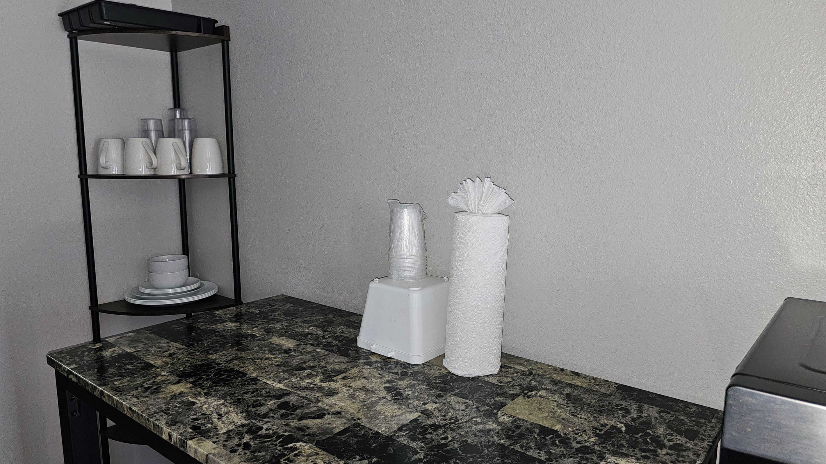 Et badeværelse med en marmorbordplade, en sort metalreol med toiletartikler og en håndklædedispenser.