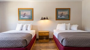 Habitación de hotel con dos camas, una mesita de noche y dos lámparas de pared.