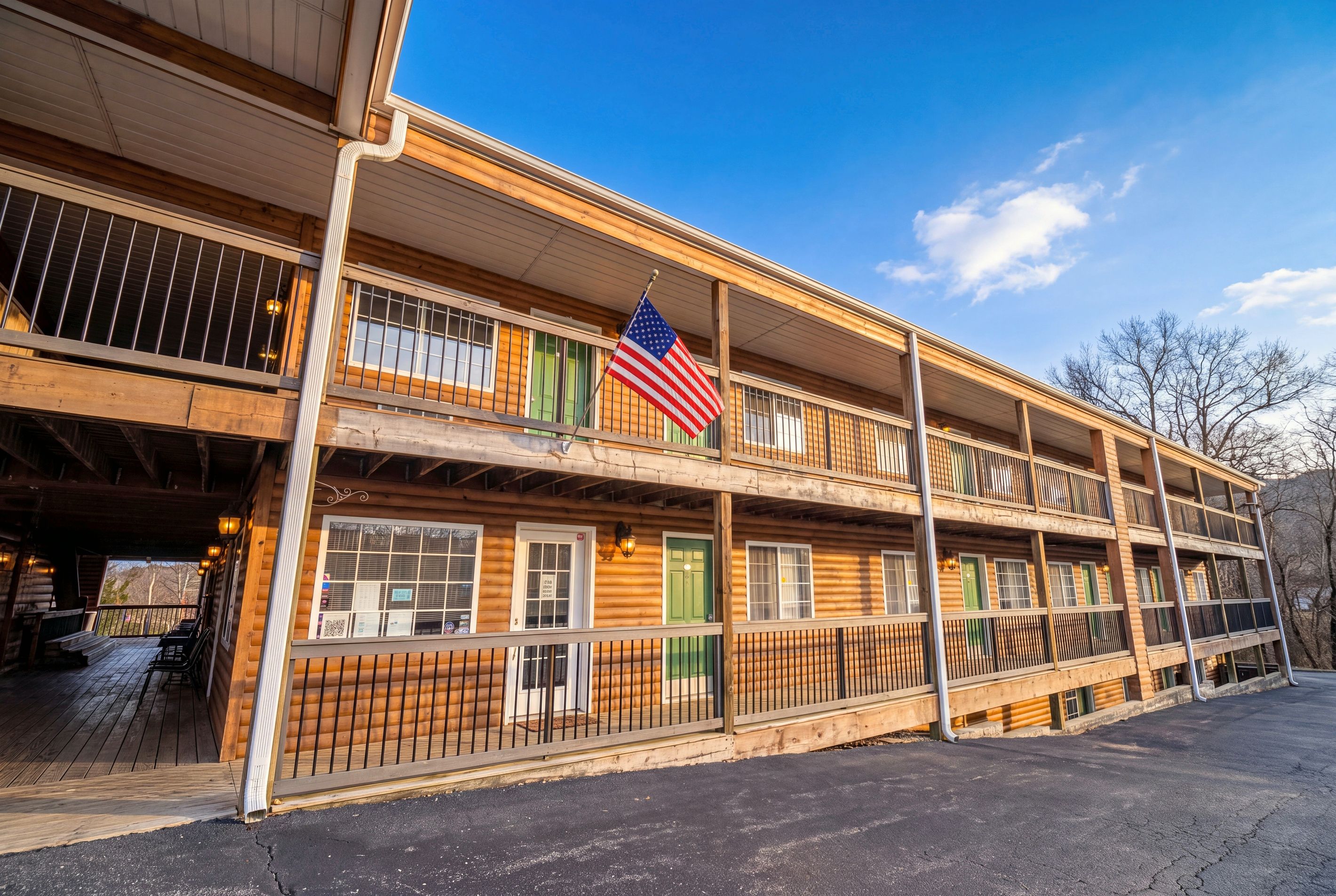 A multi-story log cabin with a balcony, an American flag, and a wooden exterior.