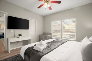 A bedroom with a bed, a desk, a television, and a window with blinds. - 2 Private Homes | 5BR 3.5BA Sleeps 18 | Fire Pit + 2 BBQs | 15 Mins to Downtown (Austin)