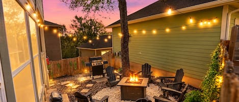 An outdoor patio with a fire pit, seating, and string lights.