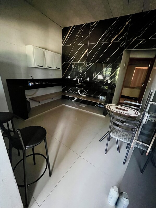 A modern kitchen with a black marble backsplash, white cabinets, and a small dining area with a round table and chairs. - Urban Hospedagem Almenara (Almenara)