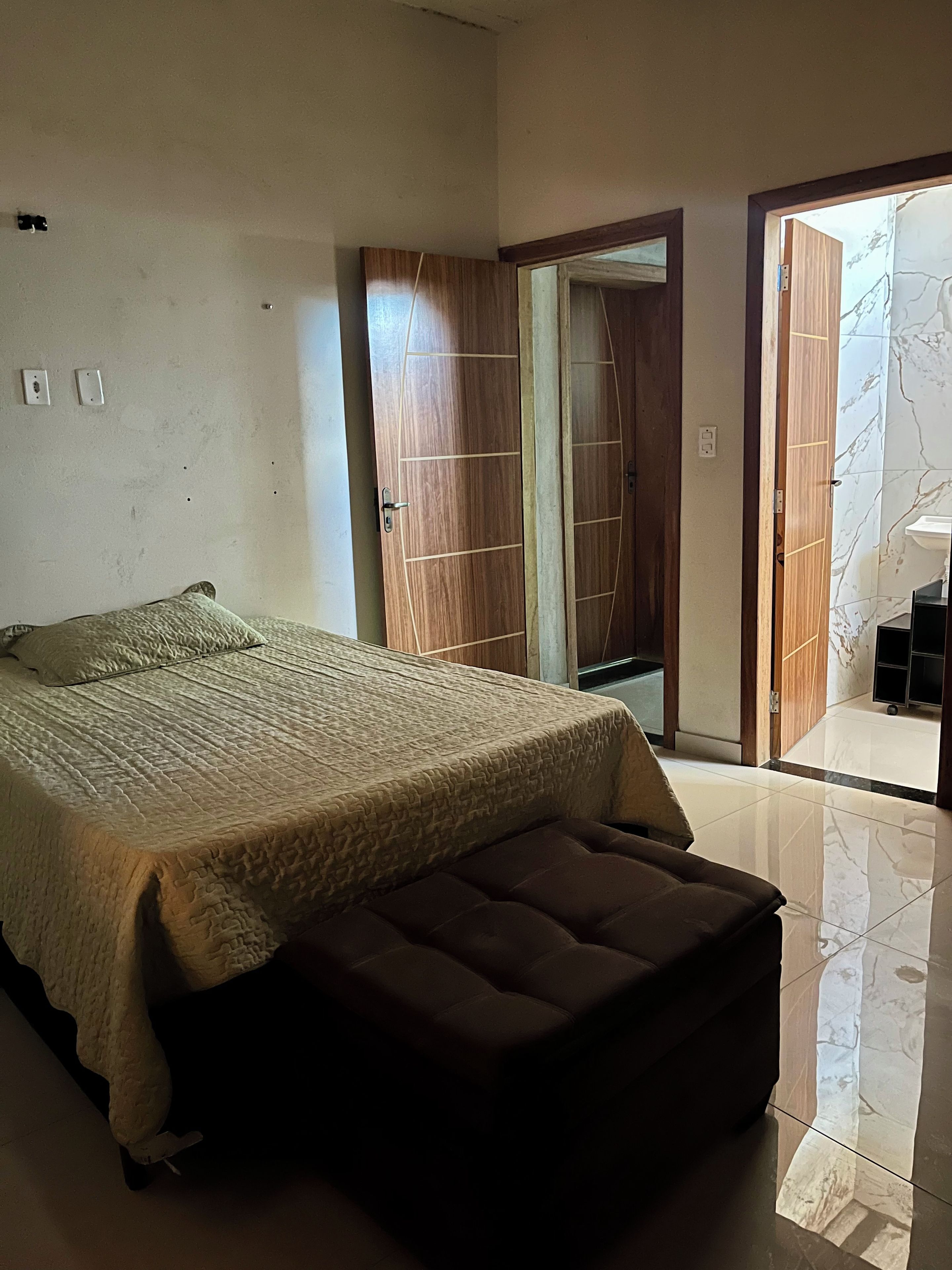 Een slaapkamer met een bed, een bankje, een kledingkast en een badkamer zichtbaar door een geopende deur.