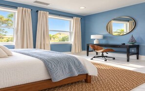 Ein Schlafzimmer mit einem Bett, einem Schreibtisch, einem Stuhl, einem runden Spiegel und Blick ins Freie.