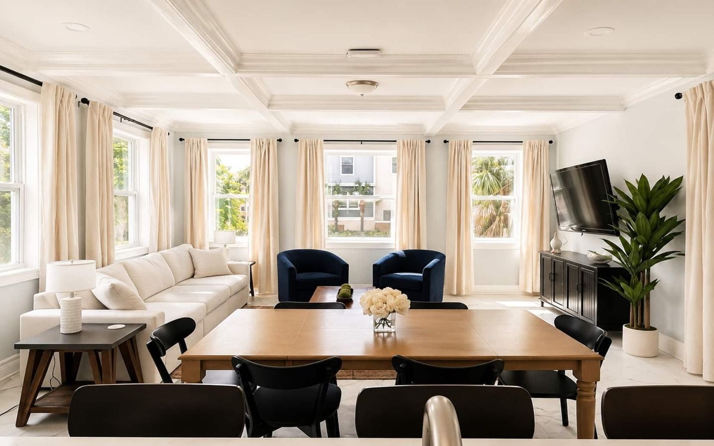 Une salle à manger moderne avec une grande table, des chaises noires, un canapé et un téléviseur fixé au mur.