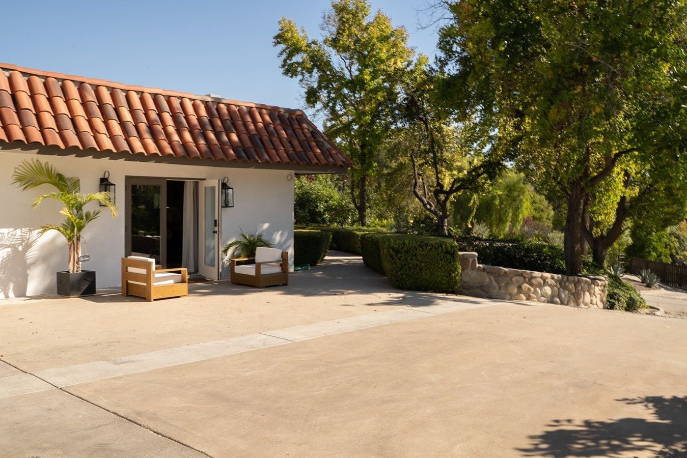 A house with a tiled roof, a paved driveway, and a well-maintained garden with a stone wall and trimmed hedges.