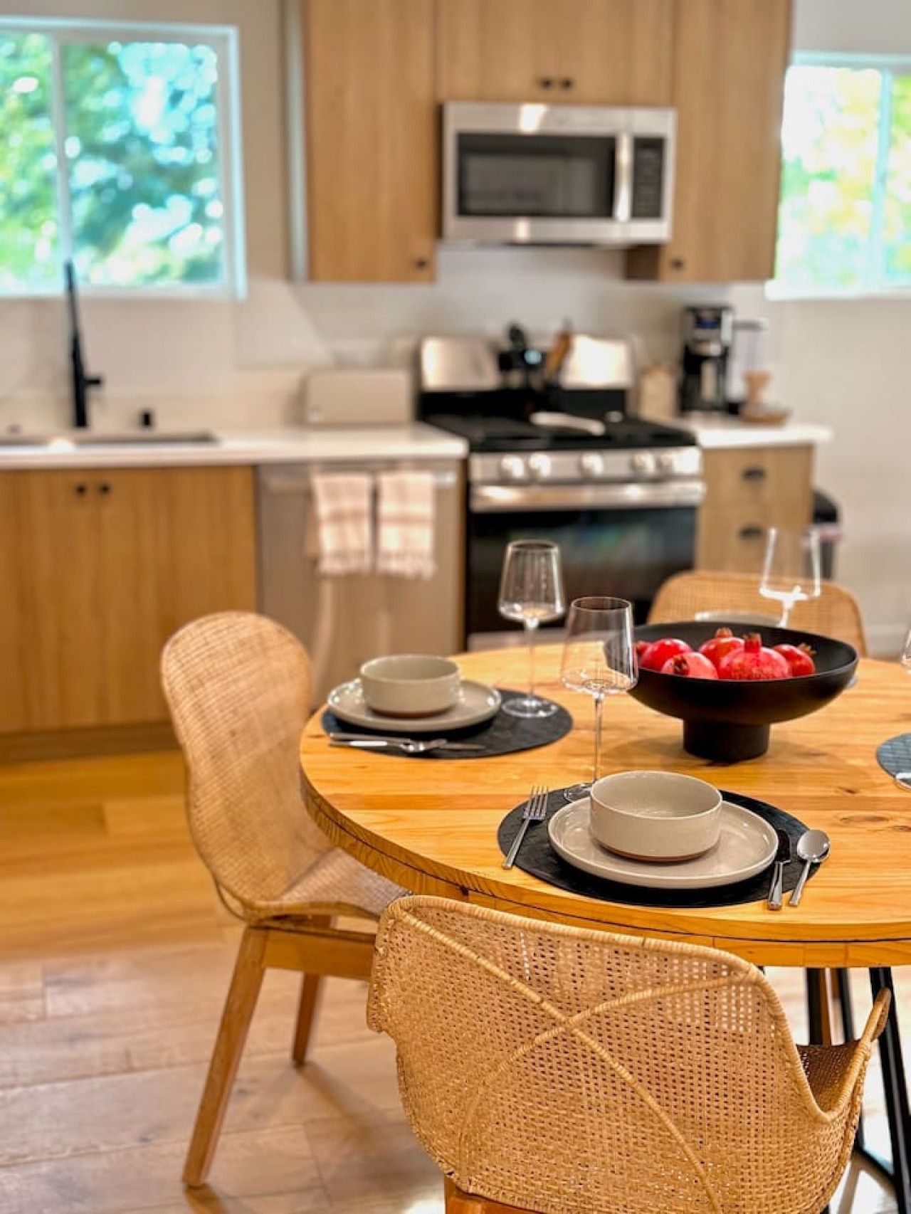 A modern kitchen with wooden cabinets, a microwave, and a stove. There is a dining table with chairs and a bowl of fruit.