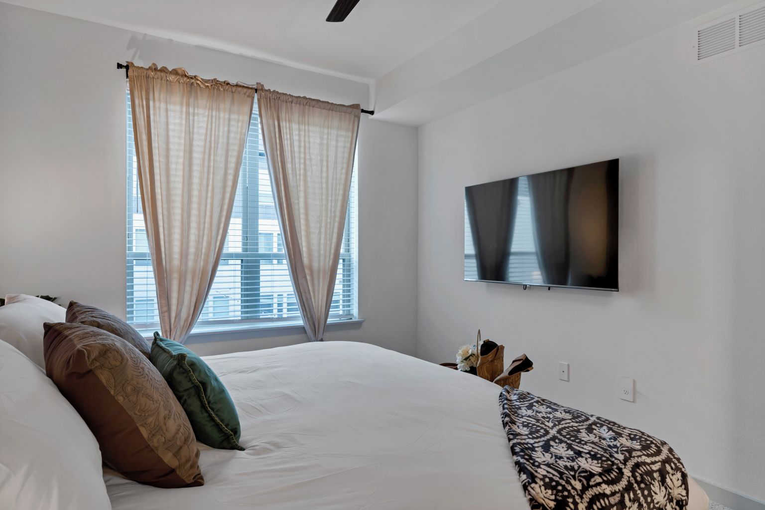 A hotel room with a large bed, a flat-screen TV, and a window with curtains.