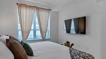 A hotel room with a large bed, a flat-screen TV, and a window with curtains.