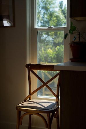 Ein Holzstuhl mit gewobener Sitzfläche steht an einem Fenster mit Blick auf Bäume.