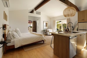 A modern bedroom with a large bed, a small desk, and a view of the outdoors.