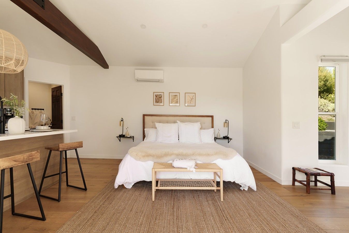 Un dormitorio con cama, mesitas de noche, un banco, una lámpara colgante y una ventana.