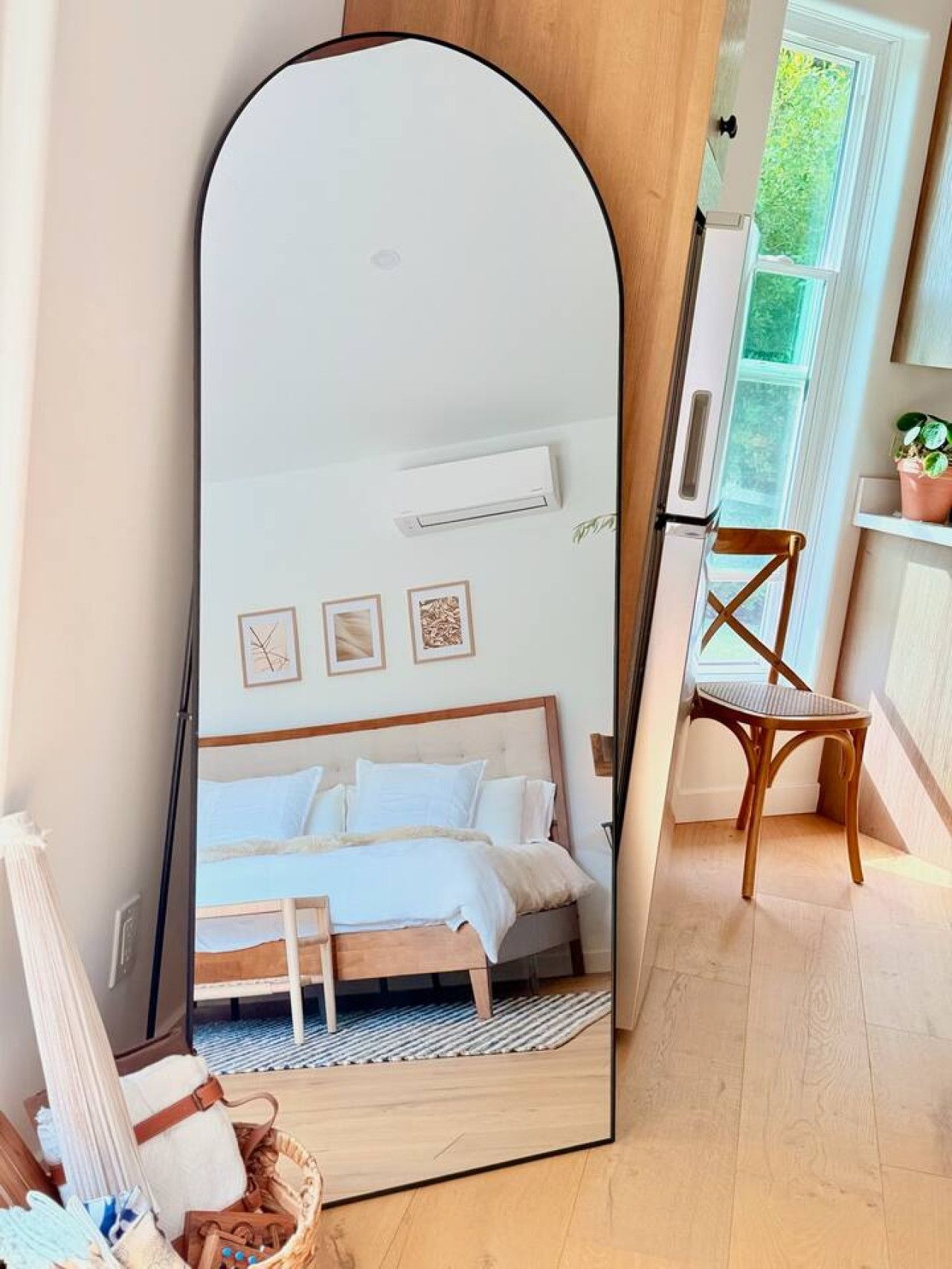 A bedroom with a large mirror, a bed, a chair, and a window with a view of greenery.