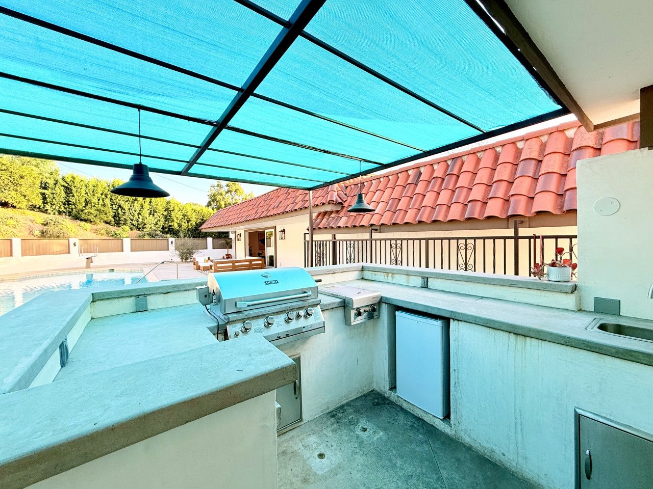 Ein Outdoor-Kochbereich mit Grill, Spüle und überdachter Terrasse.