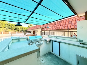 Ein Outdoor-Kochbereich mit Grill, Spüle und überdachter Terrasse.