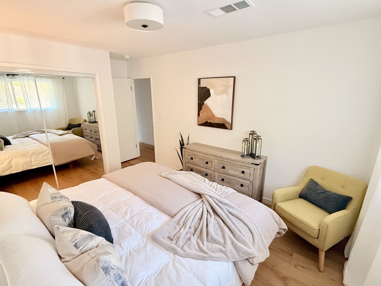 Ein modernes Schlafzimmer mit einem großen Bett, einem Sessel, einer Kommode und einem Gemälde an der Wand.