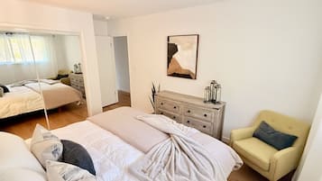 Ein modernes Schlafzimmer mit einem großen Bett, einem Sessel, einer Kommode und einem Gemälde an der Wand.