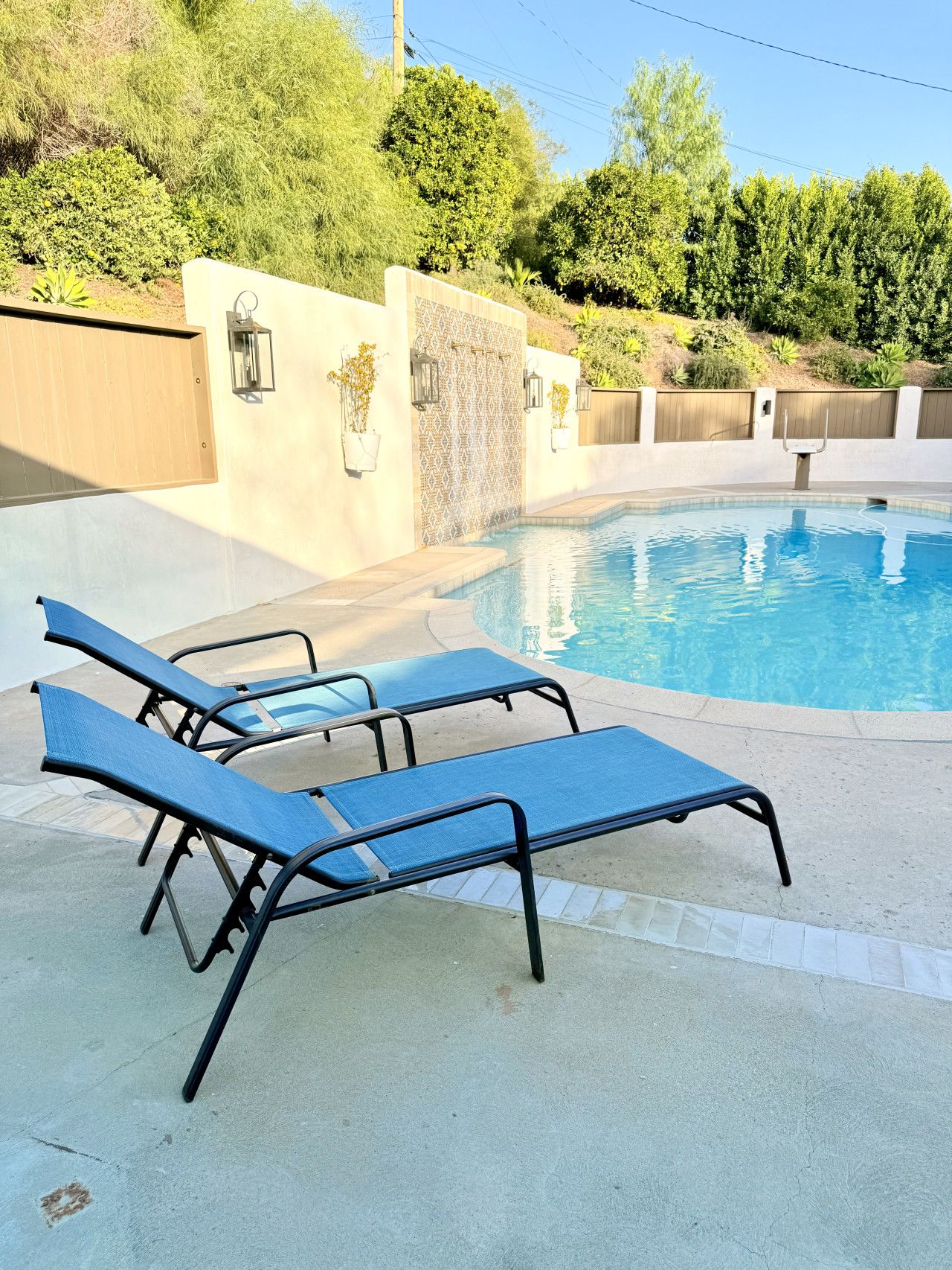 A swimming pool with three lounge chairs and a stone wall with a patterned design.