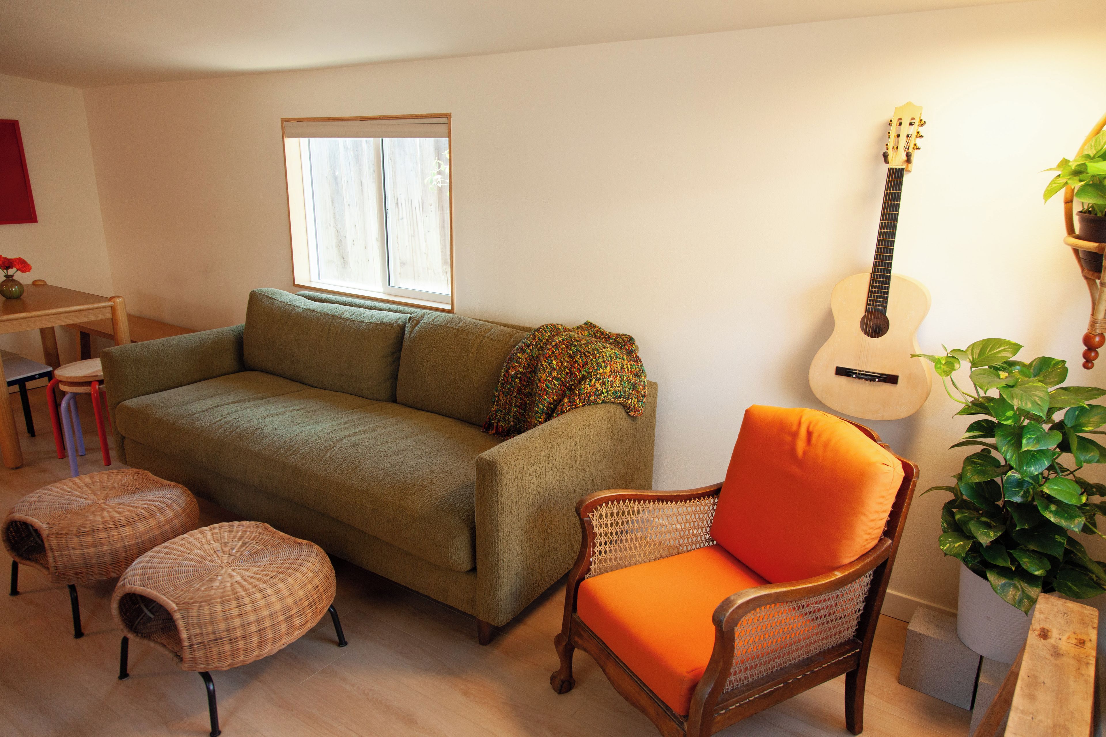 A living room with a sofa, a chair, a guitar, and a window.