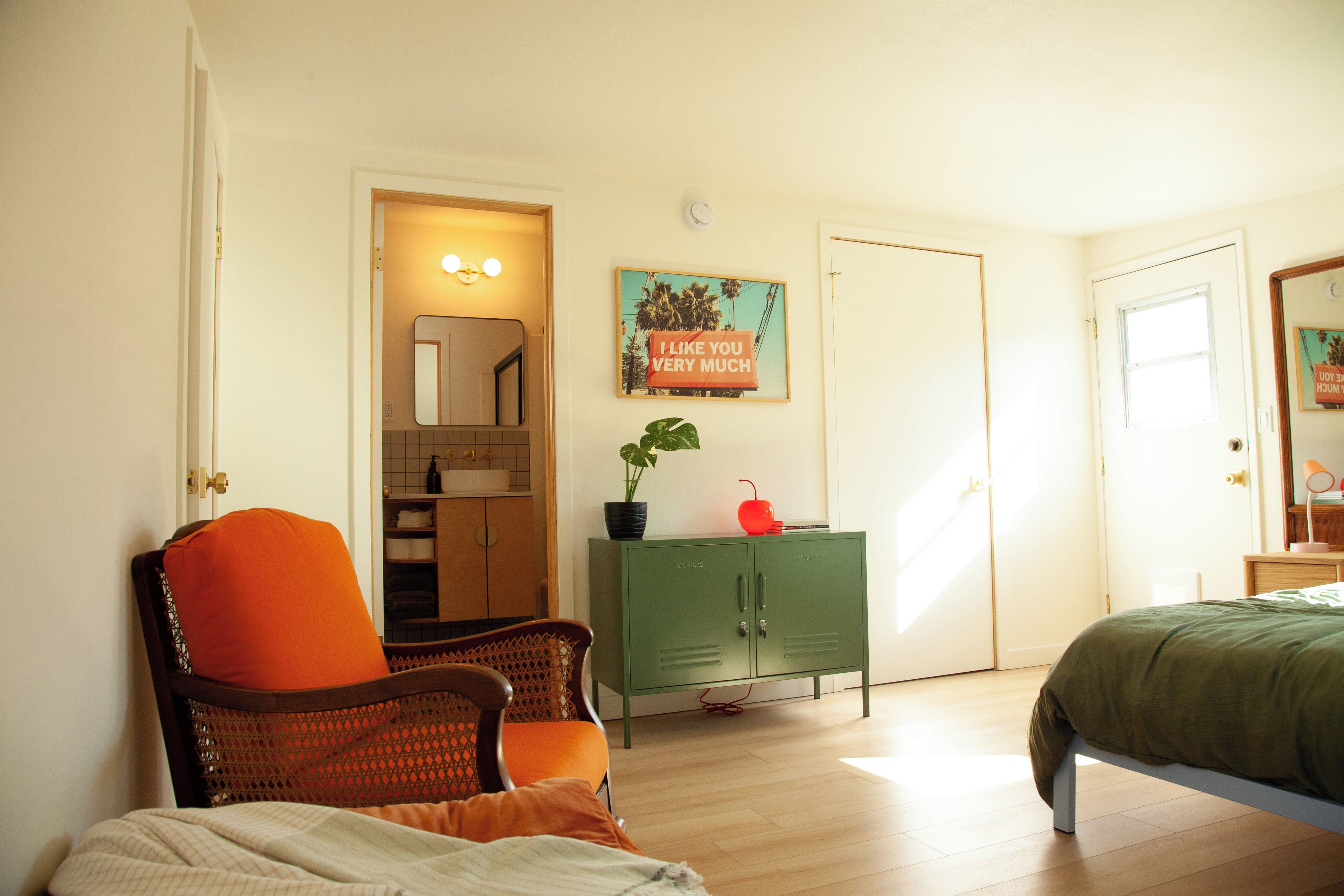 A bedroom with a bed, a chair, a dresser, and a door leading to a bathroom.
