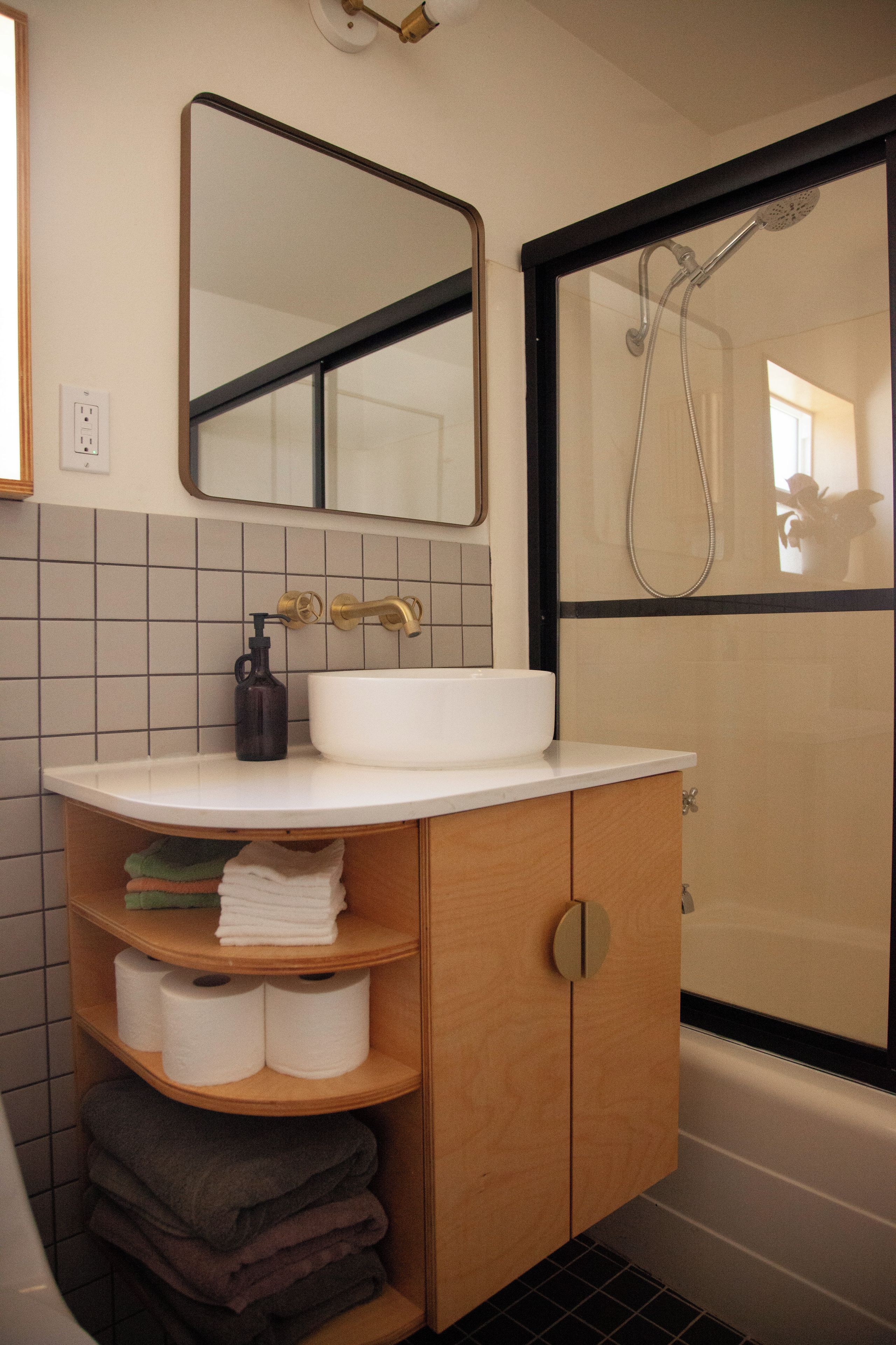 Een badkamer met een witte wasbak, een spiegel erboven, een handdoekrek met handdoeken, en een douche met een glazen deur.