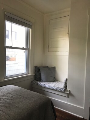 Ein Zimmer mit einem Bett, einem Fenster und einer eingebauten Sitzbank mit Kissen.