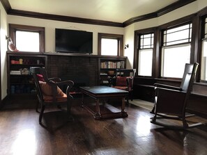 A room with a fireplace, a television mounted above it, a bookshelf, and a rocking chair. - Tranquil 4-bedroom house 2 miles from ND (South Bend)
