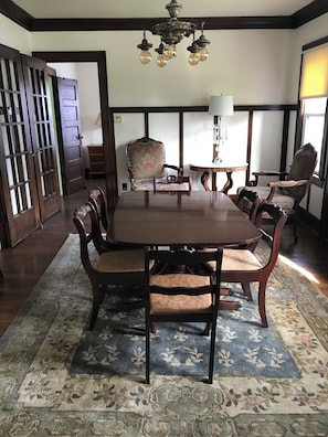 Uma sala de jantar com mesa e cadeiras de madeira, um lustre e um tapete estampado.