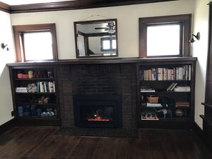 Ein Kamin mit Feuer, flankiert von Bücherregalen an beiden Seiten, und ein Spiegel darüber.