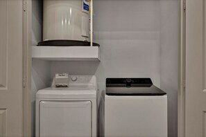 Une buanderie équipée d’un lave-linge et d’un sèche-linge à chargement frontal, d’un four à micro-ondes placé au-dessus du sèche-linge et d’une petite étagère sur laquelle se trouve une boîte étiquetée « Feuilles pour sèche-linge ».